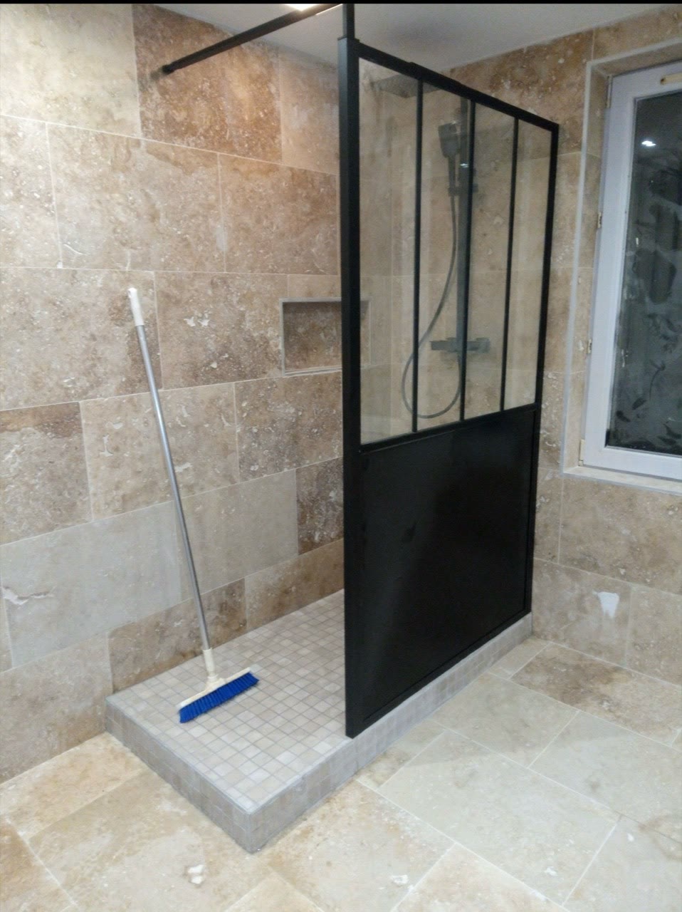 Douche carrelée dans des tons pierre avec paroi vitrée noire